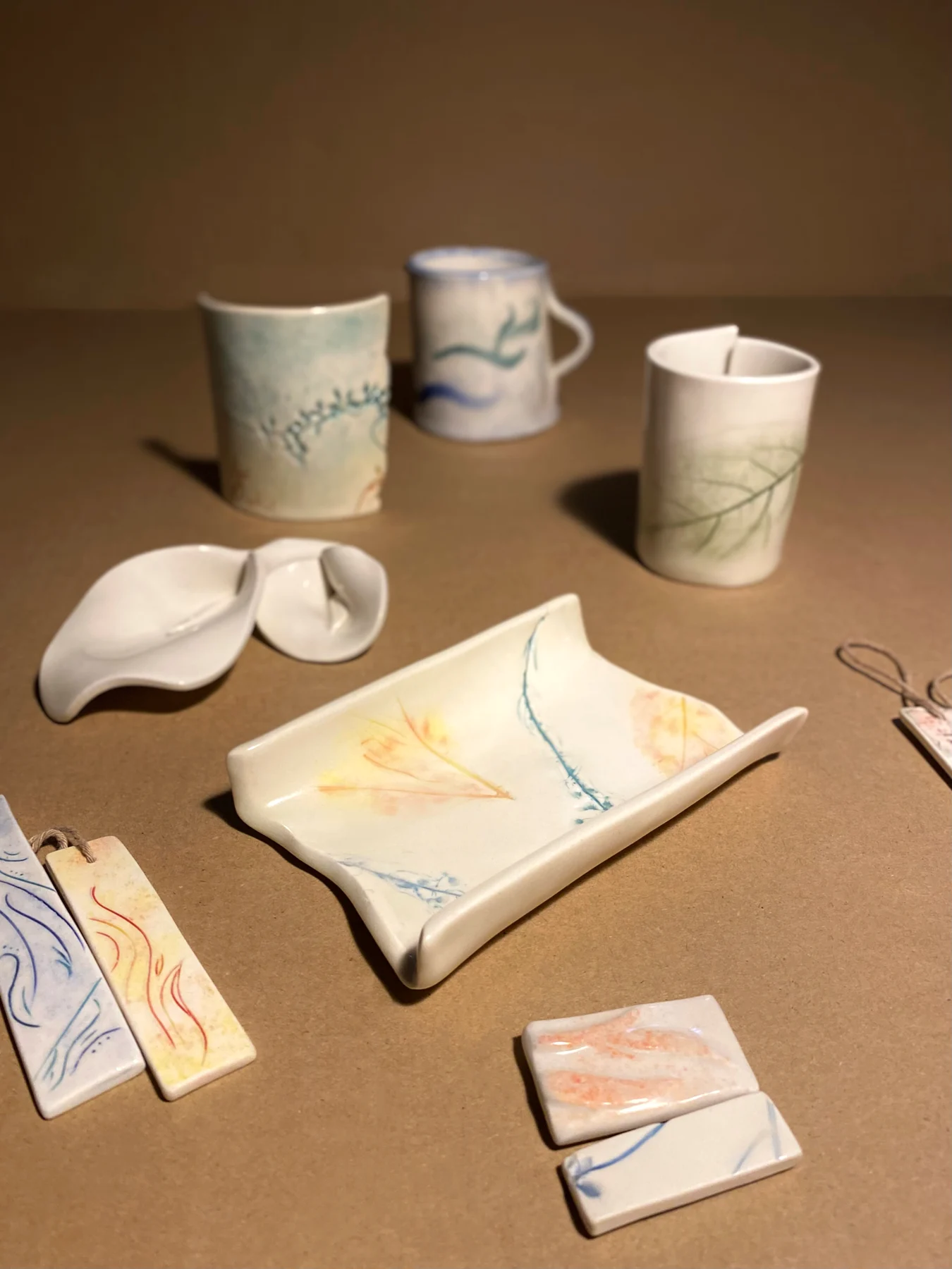 Handbuilt mugs and plates displayed with smaller ceramic pieces